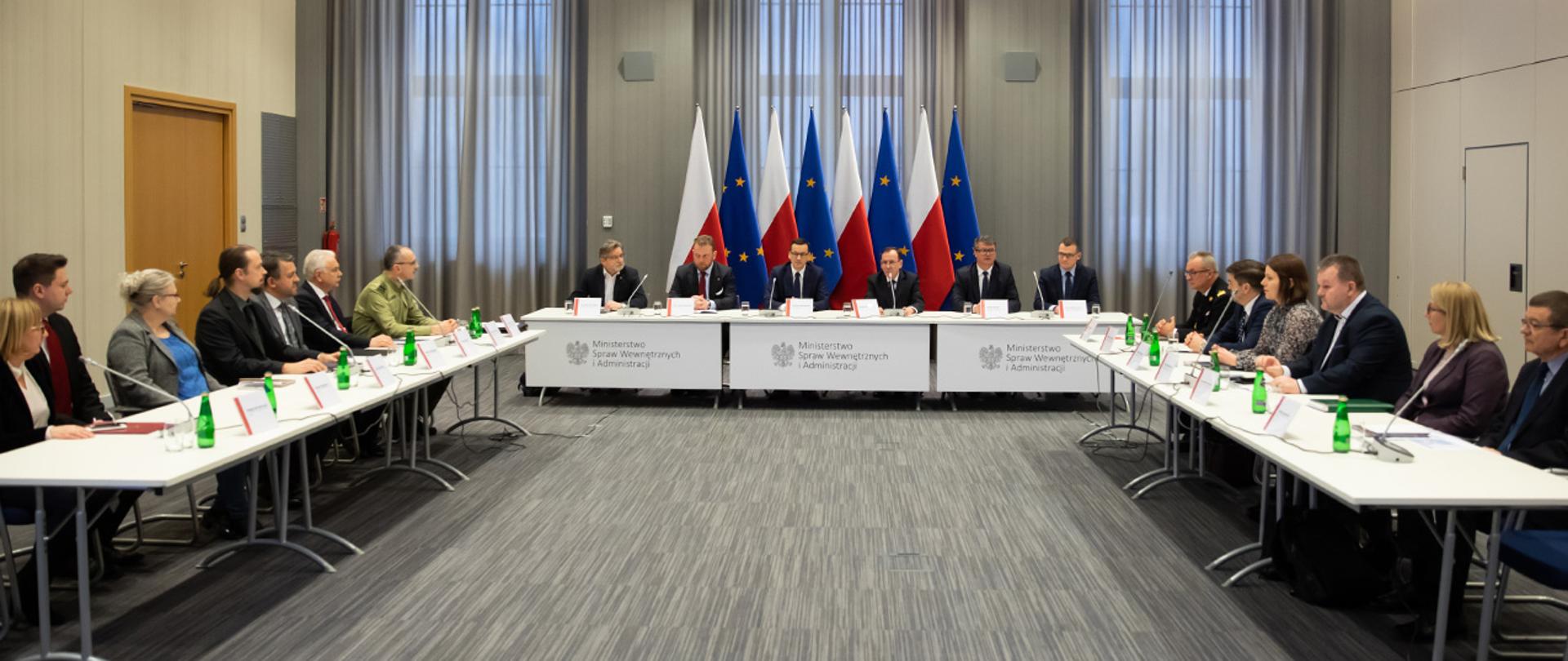 Na zdjęciu widać siedzących za stołami m.in. premiera Mateusza Morawieckiego, ministra Mariusza Kamińskiego, ministra zdrowia Łukasza Szumowskiego, wiceministra Macieja Wasika, wiceministra Pawła Szefernakera, Jarosława Pinkasa głównego inspektora sanitarnego, gen. dyw. SG Tomasza Praga komendanta głównego SG.