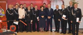Wręczenie promes. Sala sportowa w Szkaradowie. Zdjęcie grupowe strażaków z gminy Rawicz z panią minister Marlena Maląg i burmistrzem Grzegorzem Kubikiem.