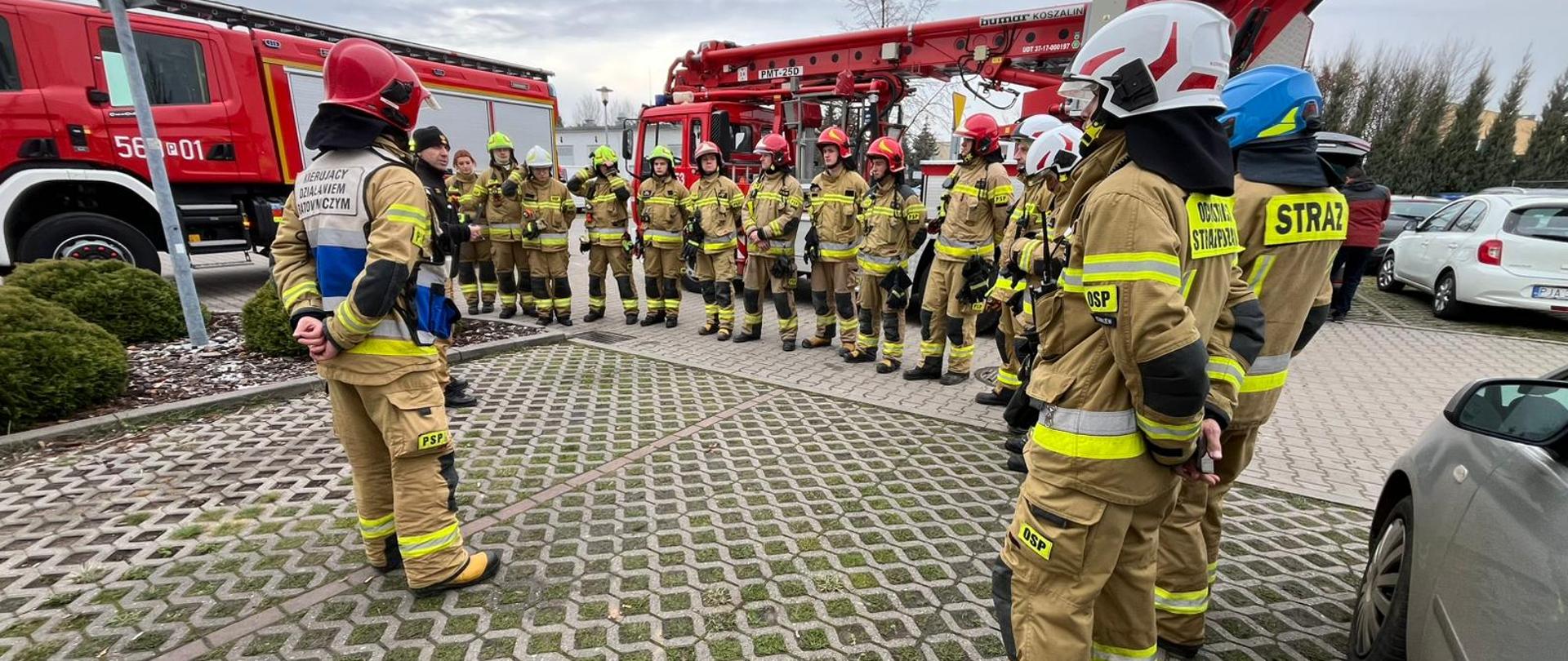 grupa osób w mundurach strażackich stojących w półokręgu na zbiórce