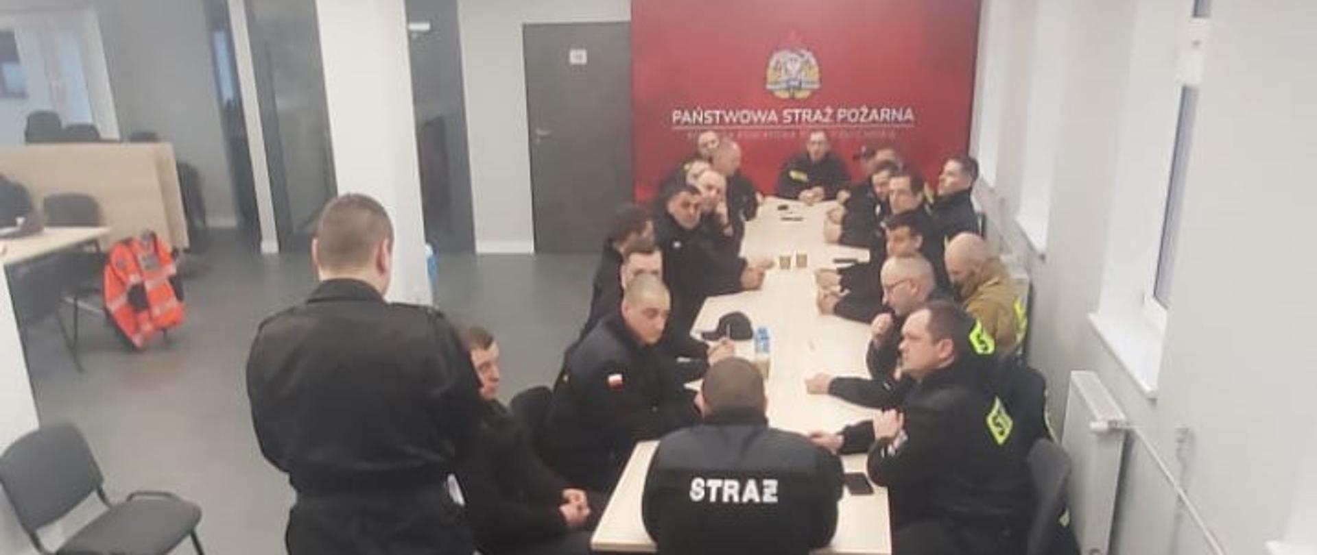 Druhowie siedzą przy stole na sali w Komendzie Powiatowej Państwowej Straży Pożarnej w Człuchowie. Przygotowanie do części teoretycznej egzaminu.