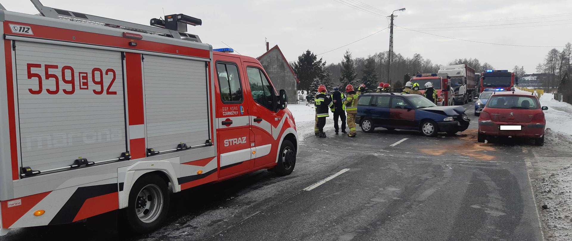 Zdjęcie przedstawia działania strażaków przy usuwaniu skutków kolizji dwóch samochodów osobowych, widać trzy samochody pożarnicze, radiowóz Policji