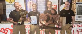 czterech strażaków z pucharem, dyplomem oraz rzeźbą stojący frontem do obiektywu
