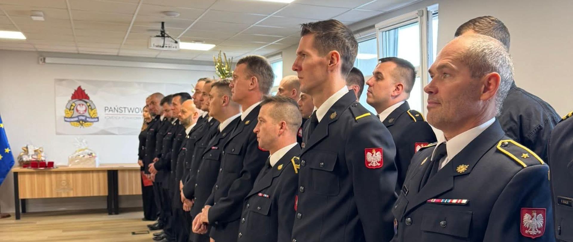 Spotkanie opłatkowe w KP PSP w Pucku. Na zdjęciu widać funkcjonariuszy ustawionych w dwuszeregu. Ubrani są w mundury galowe. 