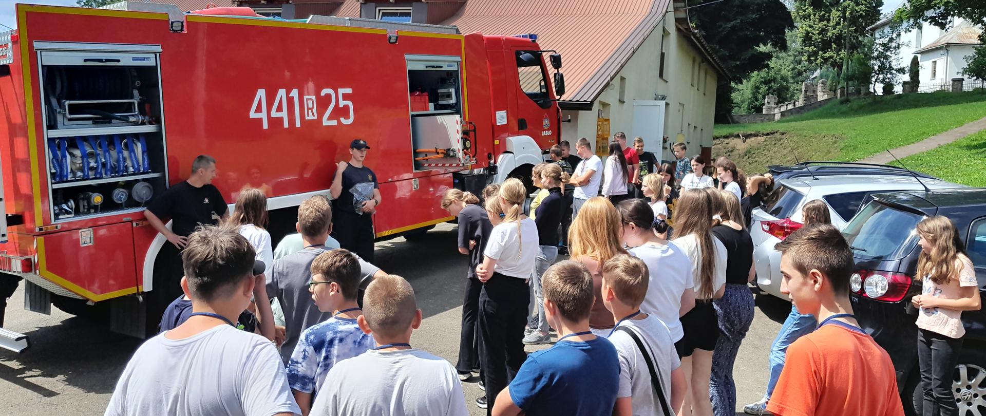 Na zdjęciu samochód strażacki a wokoło zgromadzona młodzież, na tle wozu strażackiego młodszy kapitan Paweł Zimoń, ogniomistrz Grzegorz Szot. 