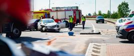 Na zdjęciu widoczni są funkcjonariusze policji oraz uszkodzony w wyniku zdarzenia samochód osobowy. Na drugim planie widoczny jest samochód ratowniczo gaśniczy oraz karetka pogotowia.