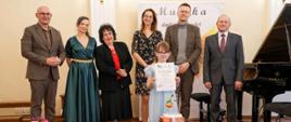 Przewodniczący Rady Powiatu, Pani Dyrektor, Jury wraz z uczestniczką podczas XII Festiwalu Polskiej Muzyki Współczesnej dla Pianistów im. Janiny Garści w Lublińcu 8-9.04.2025 r. na scenie koncertowej szkoły