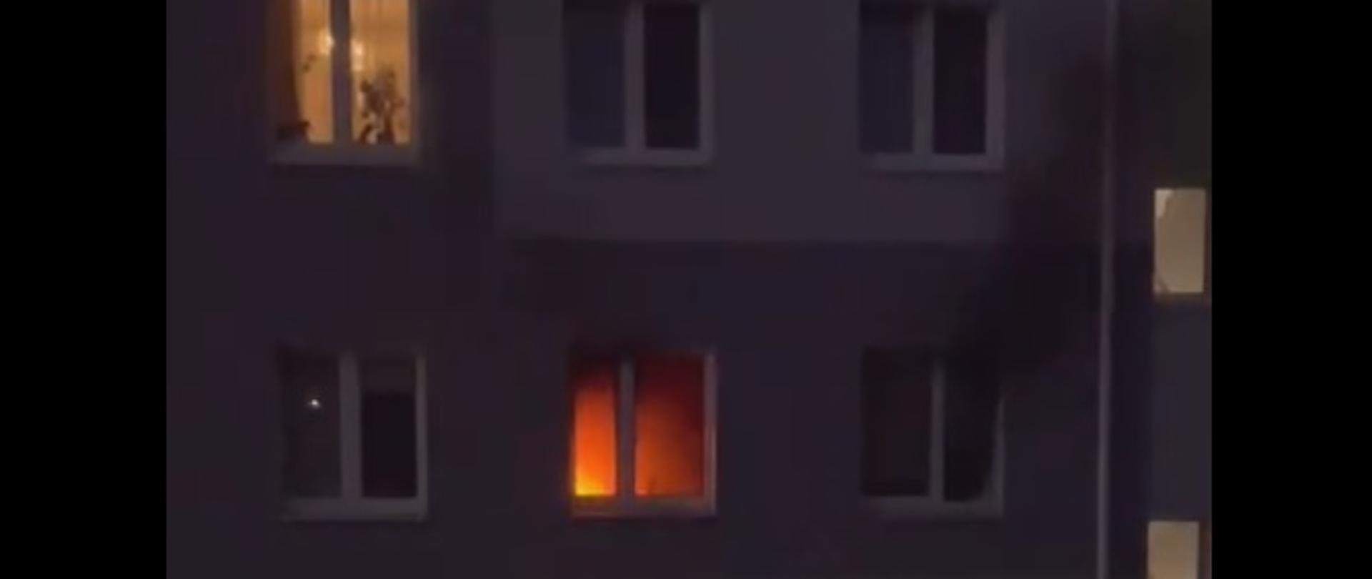 Zdjęcie przedstawia widoczne z okna płomienie oraz dym w jednym z mieszkań budynku wielorodzinnego w Gołdapi przy ulicy Szkolnej