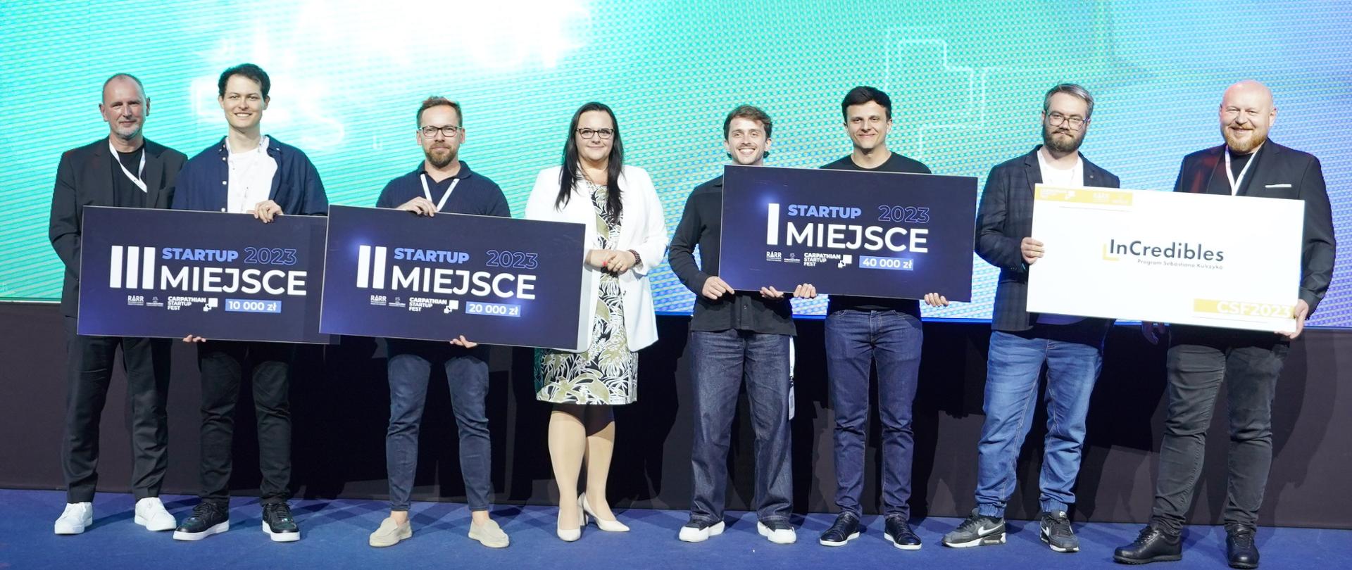 Grupa osób pozuje z symbolicznymi zwycięskimi piankami. W środku stoi wiceminister Małgorzata Jarosińska-Jedynak.