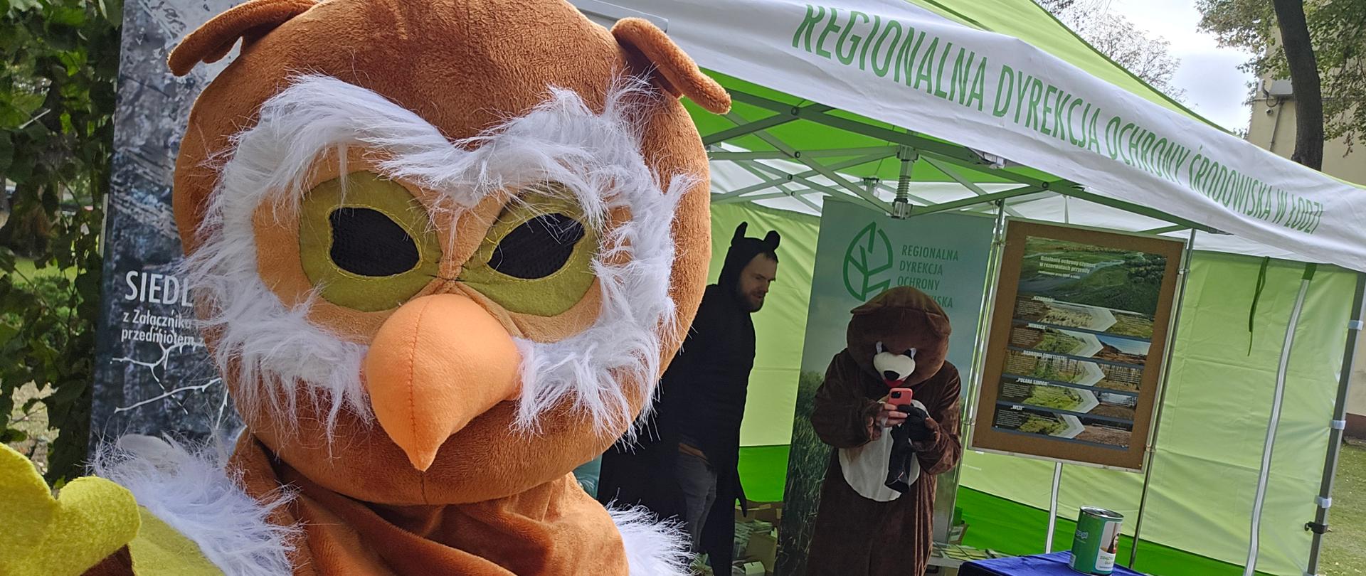 Na pierwszym tle człowiek przebrany za sowę, w oddali namiot z napisem Regionalna Dyrekcja Ochrony Środowiska w Łodzi