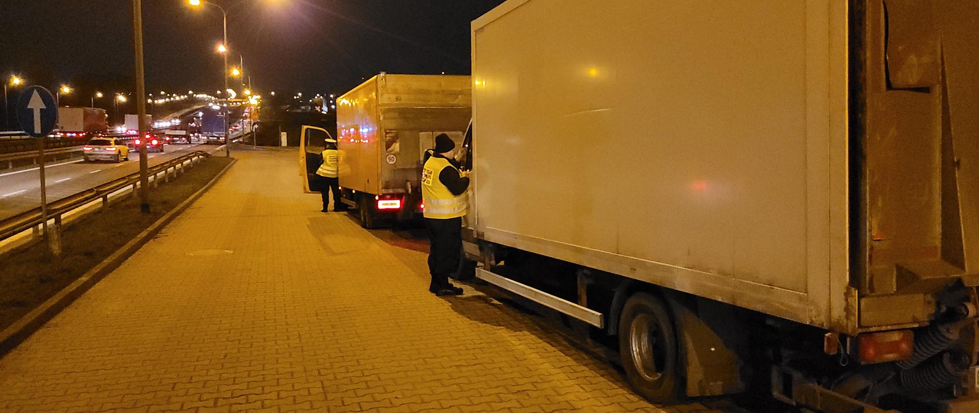 Dwie przeładowane furgonetki dostawcze stoją w punkcie kontrolnym przy drodze. Umundurowani funkcjonariusze pomorskiej Inspekcji Transportu Drogowego pobierają wymagane dokumenty od kierowców.