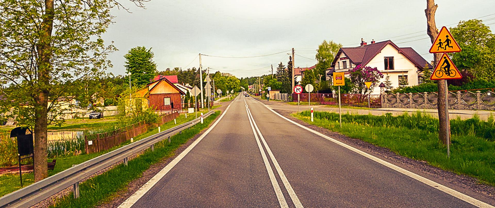 Fotografia z poziomu terenu jednoprzestrzennej drogi krajowej w gęstej zabudowie jednorodzinnej. 