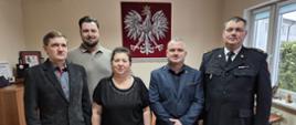 Komendant Powiatowy Państwowej Straży Pożarnej w Sępólnie Krajeńskim brygadier Marcin Mazurkiewicz w mundurze wyjściowym wraz z pracownikami cywilnymi oraz przedstawicielami związków zawodowych pozują do zdjęcia w gabinecie komendanta.