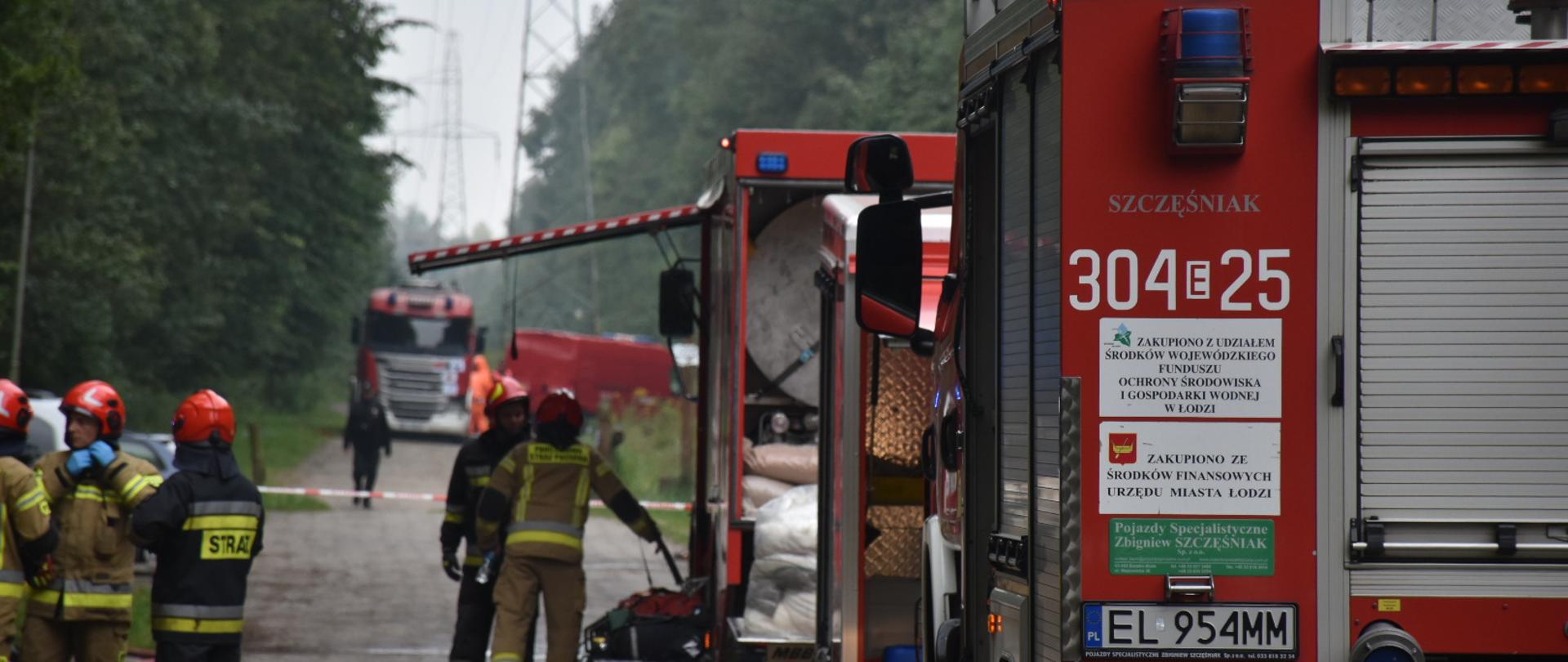 Dwa samochody ratowniczo-gaśnicze obok strażacy przygotowujący się do działań