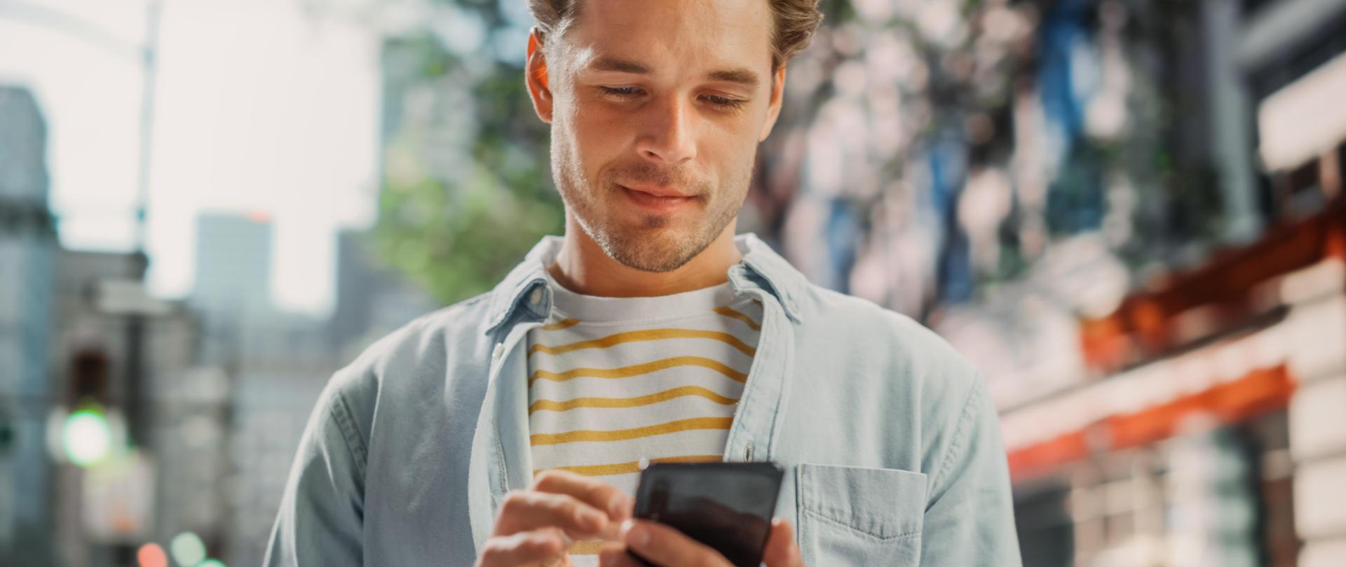 Portret młodego mężczyzny korzystającego ze smartfona na ulicy