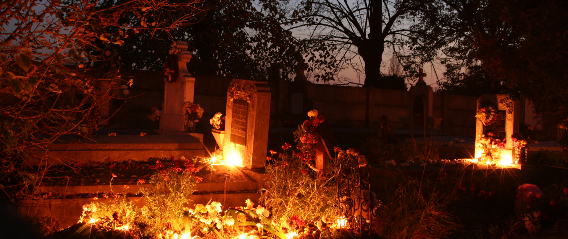 Nocne zdjęcie grobów na cmentarzu, na których palą się znicze.