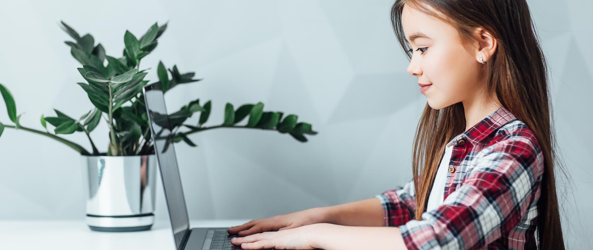 Zdjęcie w poziomie. Dziewczynka siedzi przy stole.. Przed nią stoi tablet.