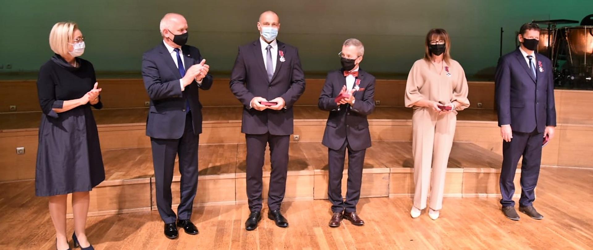 Na scenie stoi kurator oświaty, wojewoda i odznaczeni 