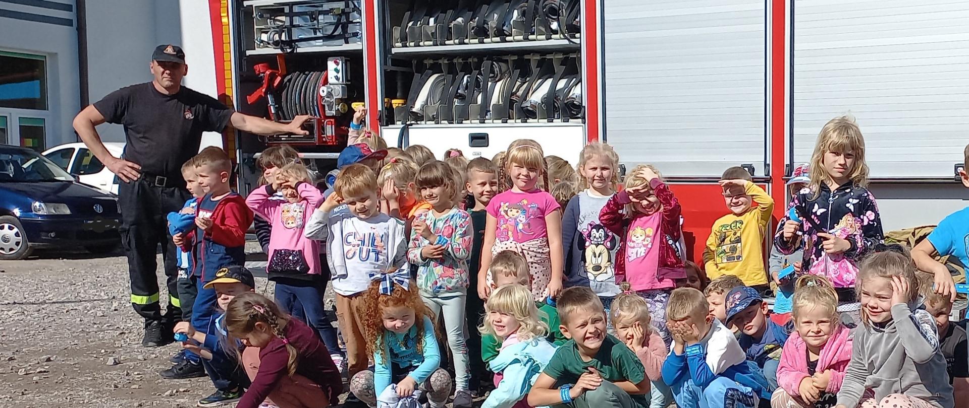 Na zdjęciu dzieci ze Szkoły podstawowej stojące przed pojazdem pożarniczym. W tle parking szkoły i samochody