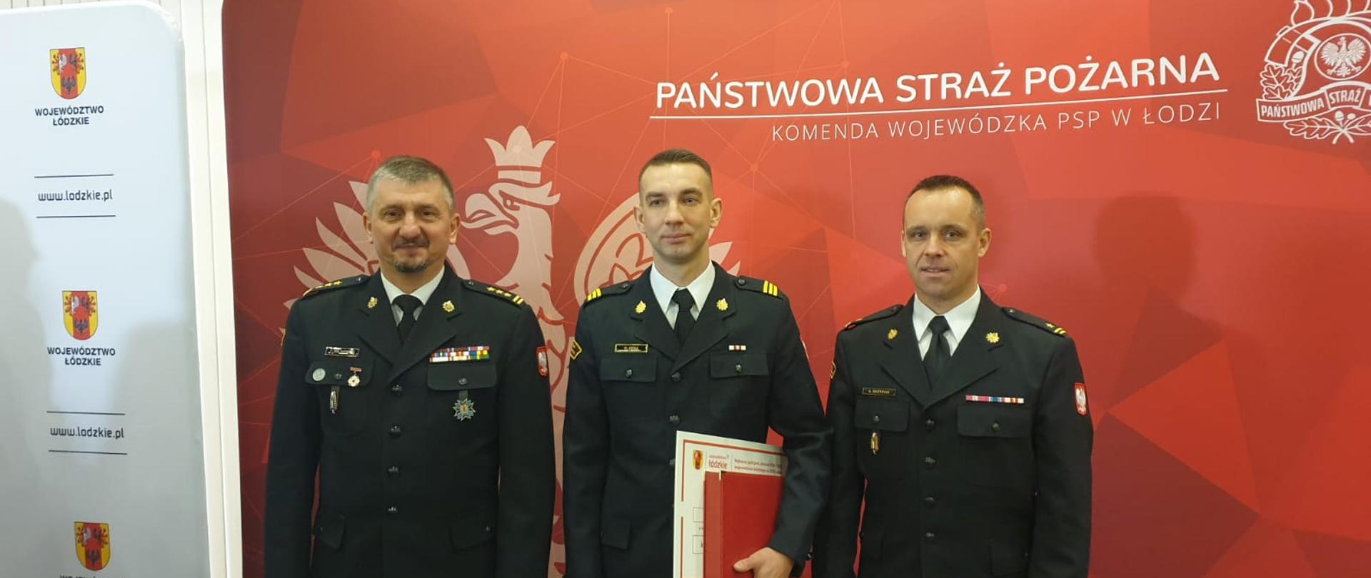 Trzej mężczyźni stojący na tle czerwonego banera. 