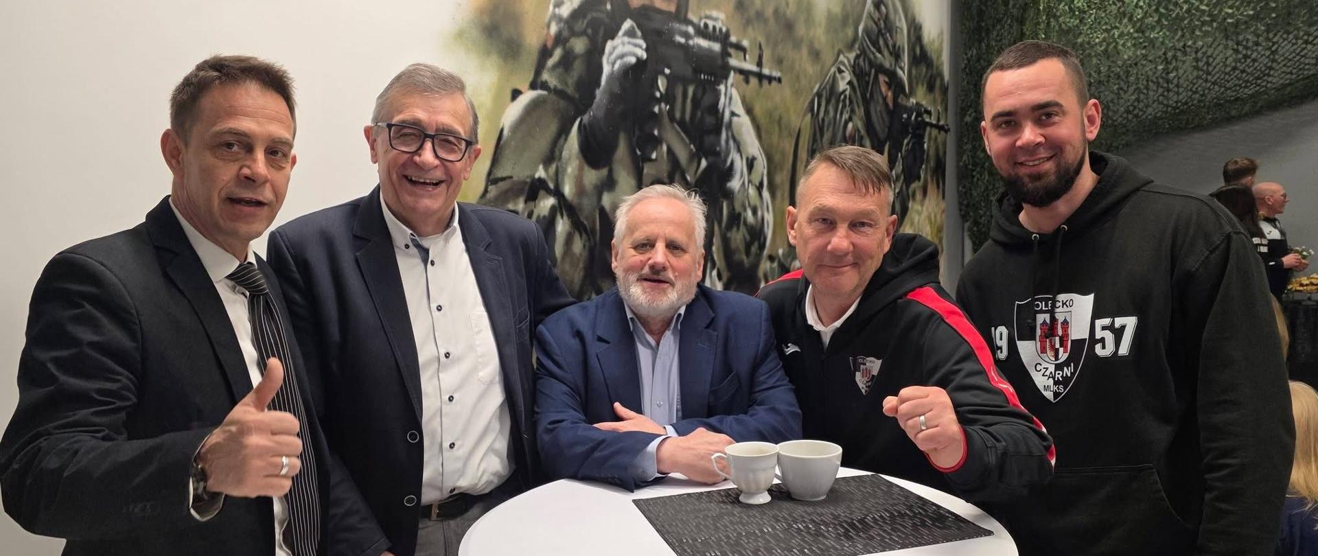 Pięciu mężczyzn stoi przy wysokim stole barowym, uśmiechają się i pozują do zdjęcia 