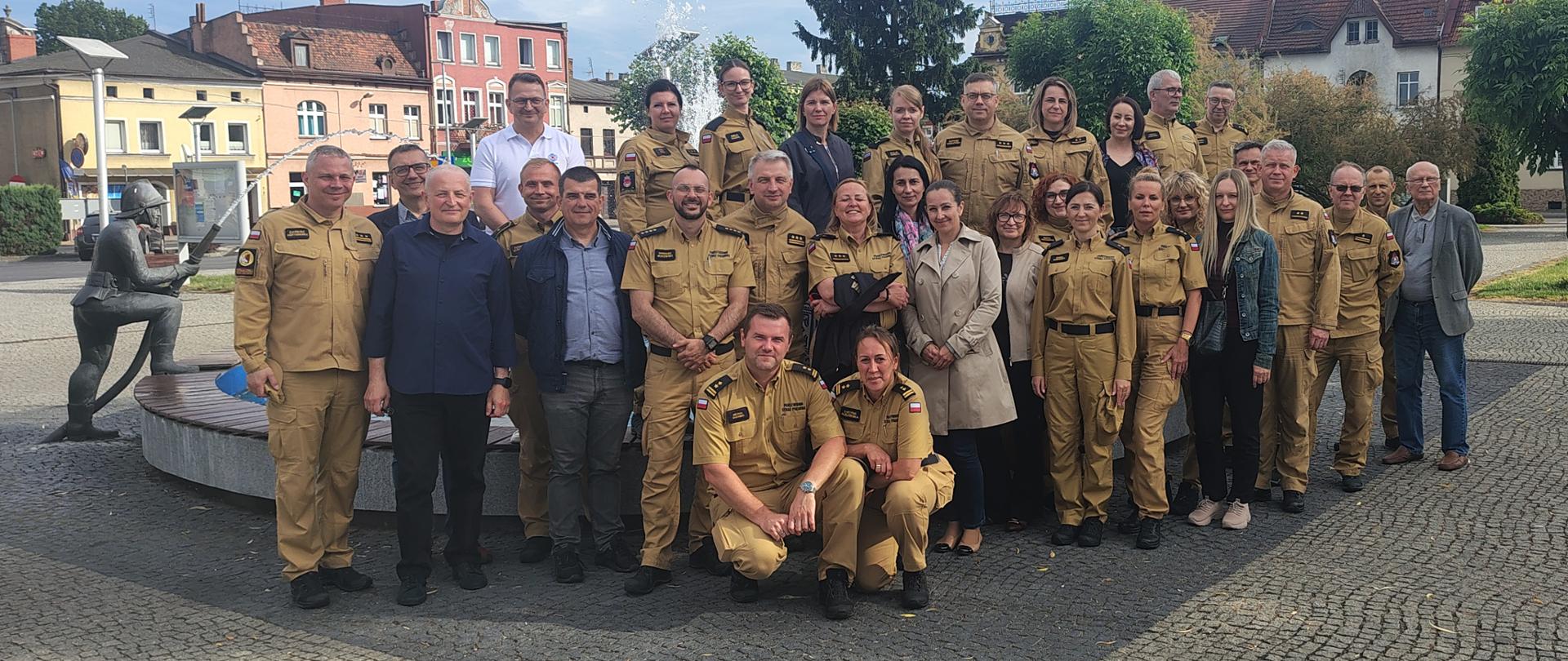 zdjęcie grupowe uczestników odprawy na tle fontanny ze strażakiem - rynek w Rakoniewicach