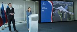 Minister funduszy i polityki regionalnej Katarzyna Pełczyńska-Nałęcz stoi przy mównicy, po jej prawej stronie stoi wiceminister Jan Szyszko, po lewej stronie pani minister stoi ekran na którym wyświetlone jest zdjęcie przedstawiające Most Rędzyński