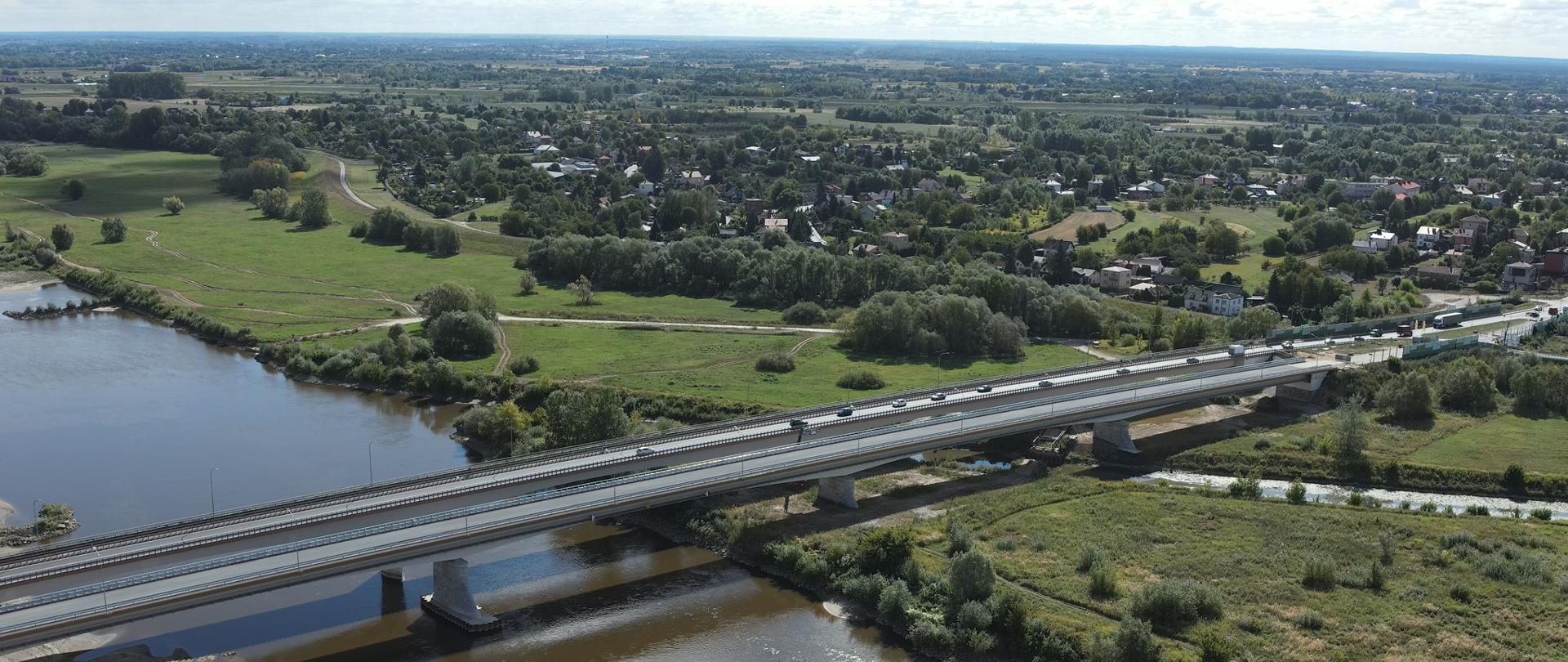 Mosty w Sandomierzu - zdjęcie z drona, nad rzeką dwa obiekty, po jednym jeżdżą pojazdy, w oddali na brzegu zieleń i domy 