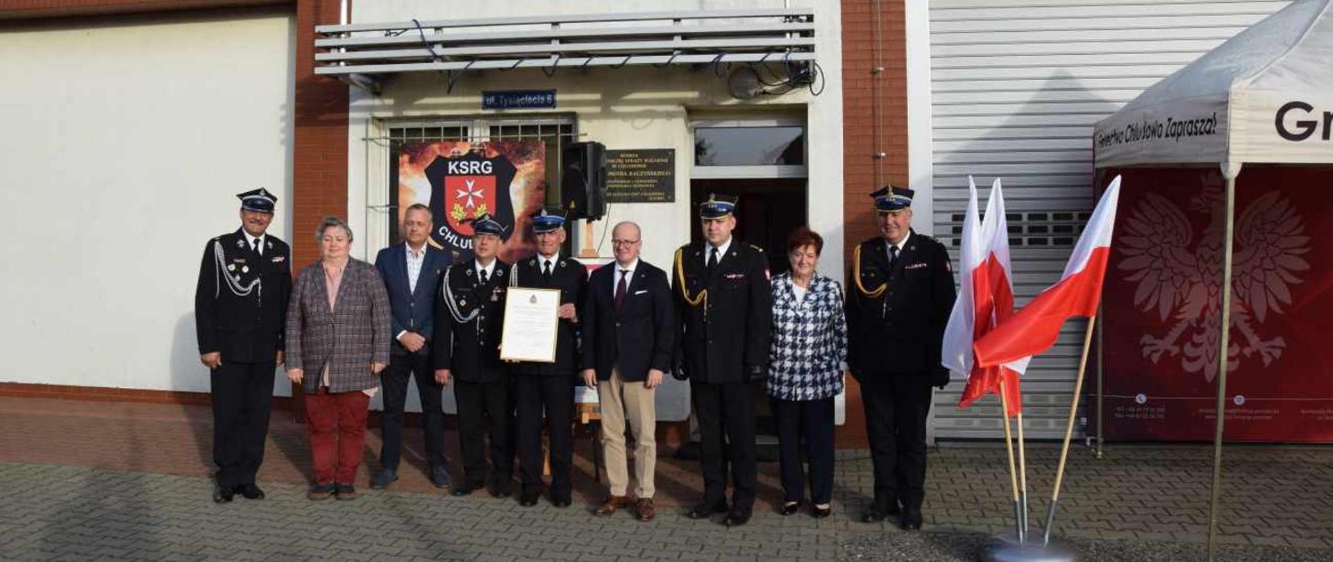 Zdjęcie przedstawia Posła, Komendantów PSP, członków OSP oraz zaproszonych gości. W tle remiza OSP.