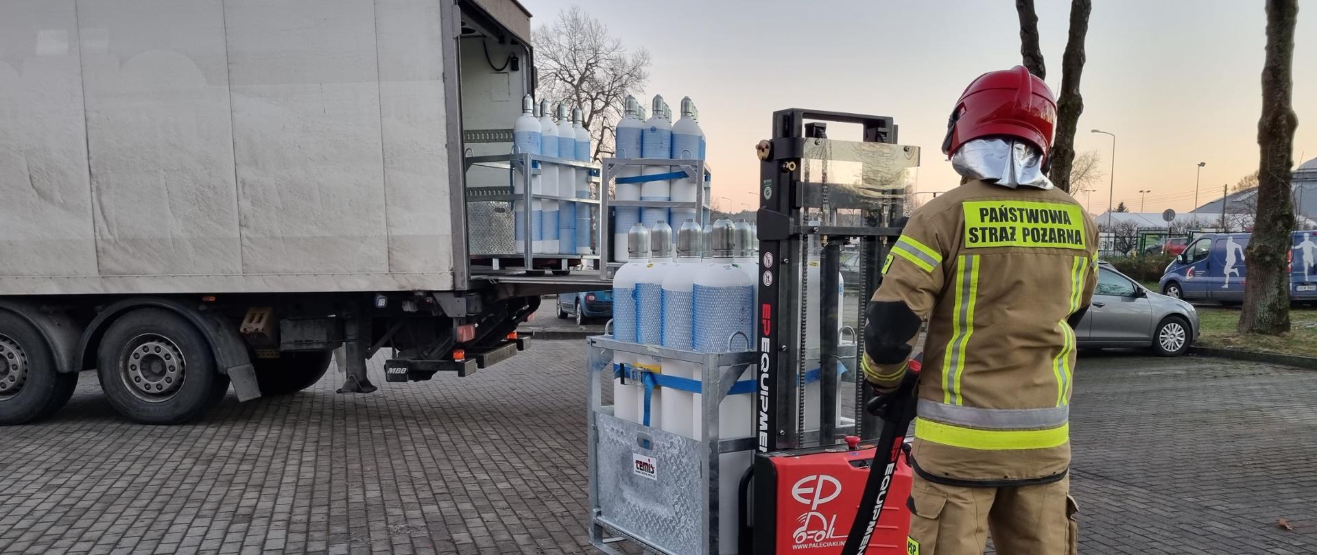 Strażak z wózkiem do przewozu palet na którym jest kontener butlami z tlenem