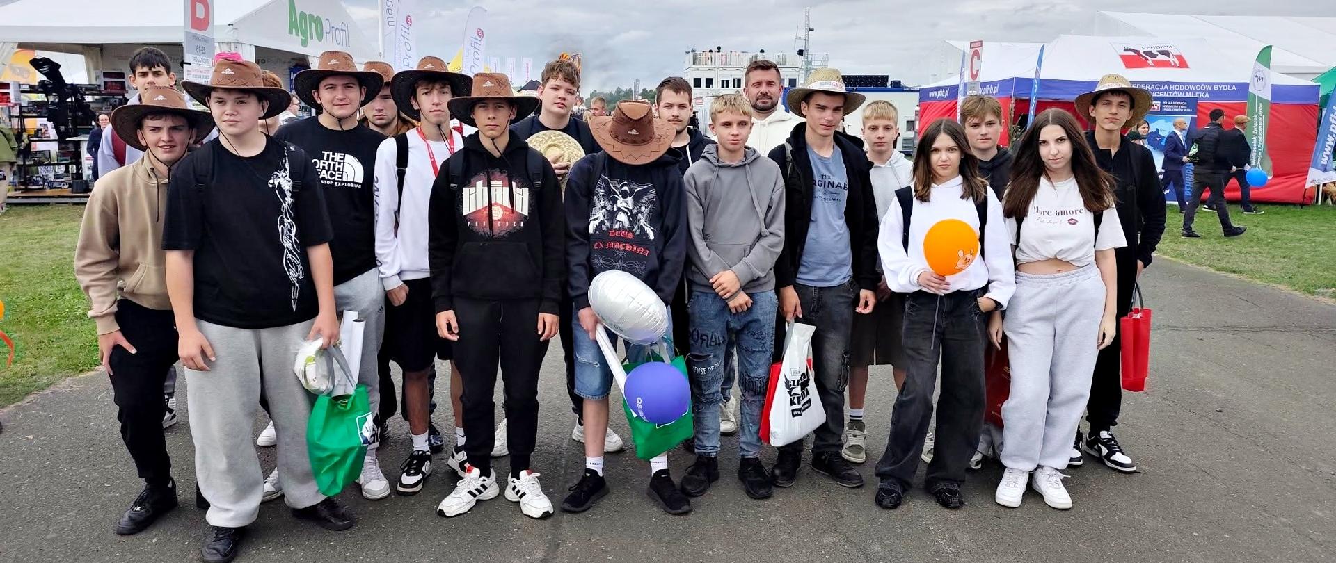 Grupa młodzieży podczas AGRO SHOW Bednary 2026. Uczestnicy w kowbojskich kapeluszach pozują do wspólnego zdjęcia na terenie międzynarodowej wystawy rolniczej, w tle widoczne są stoiska wystawców i namioty targowe. AGRO SHOW 2026 odbyło się w dniach 18–20 września 2026 r. w Bednarach koło Poznania.