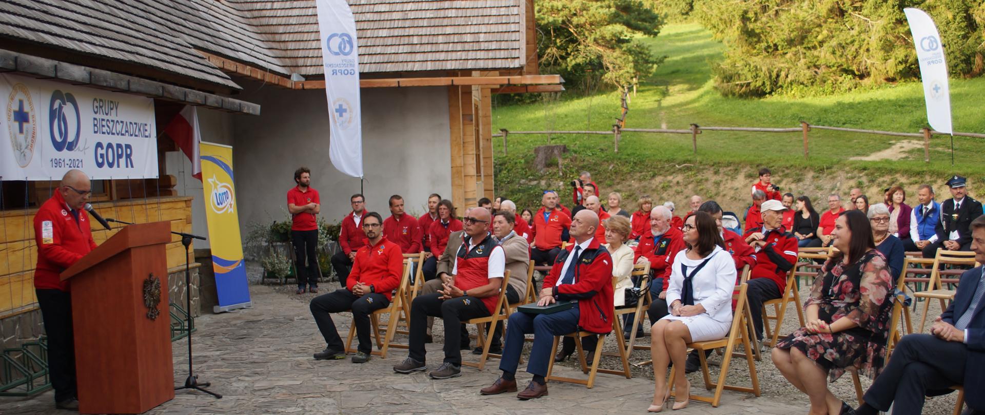 uczestnicy uroczystości siedzą wokół przemawiającego przedstawiciela Bieszczadzkiej Grupy Górskiego Ochotniczego Pogotowia Ratunkowego