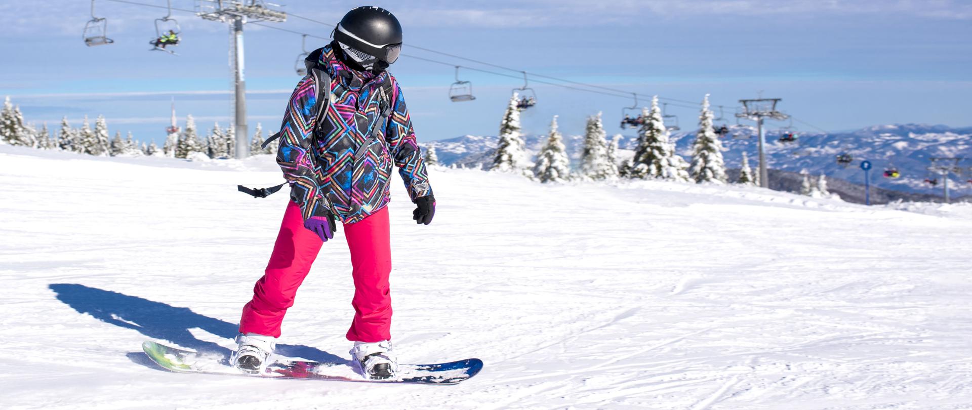 A girl learning to snowboard at a mountain resort with the ski lift in the background
