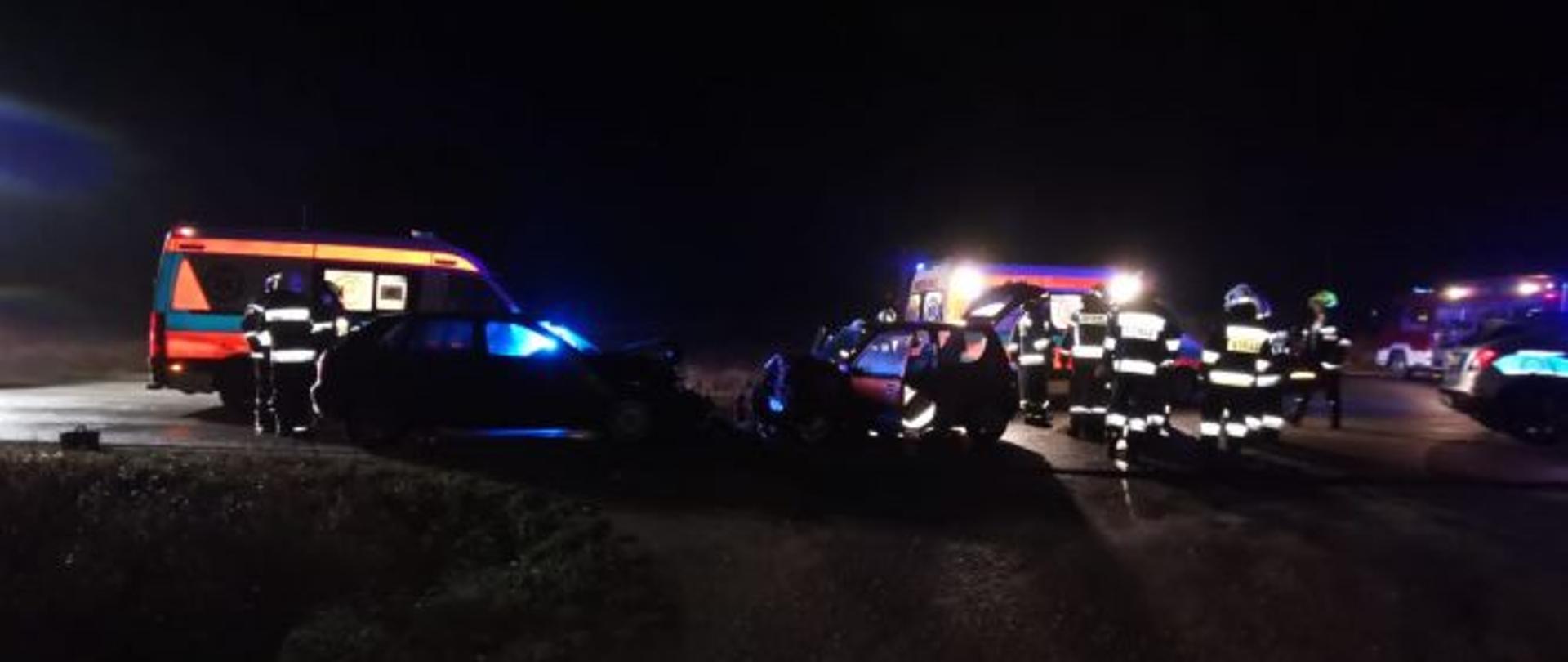 zdjęcie wykonane w porze nocnej. widać na nim cały teren akcji dwie karetki, uszkodzone pojazdy (audi i fiat seicento) strażaków . Ciemność i sztuczne oświetlenie z karetki i wozy pożarniczego. 
