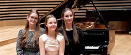 Trzy uczennice na scenie sali koncertowej, w tle fortepian