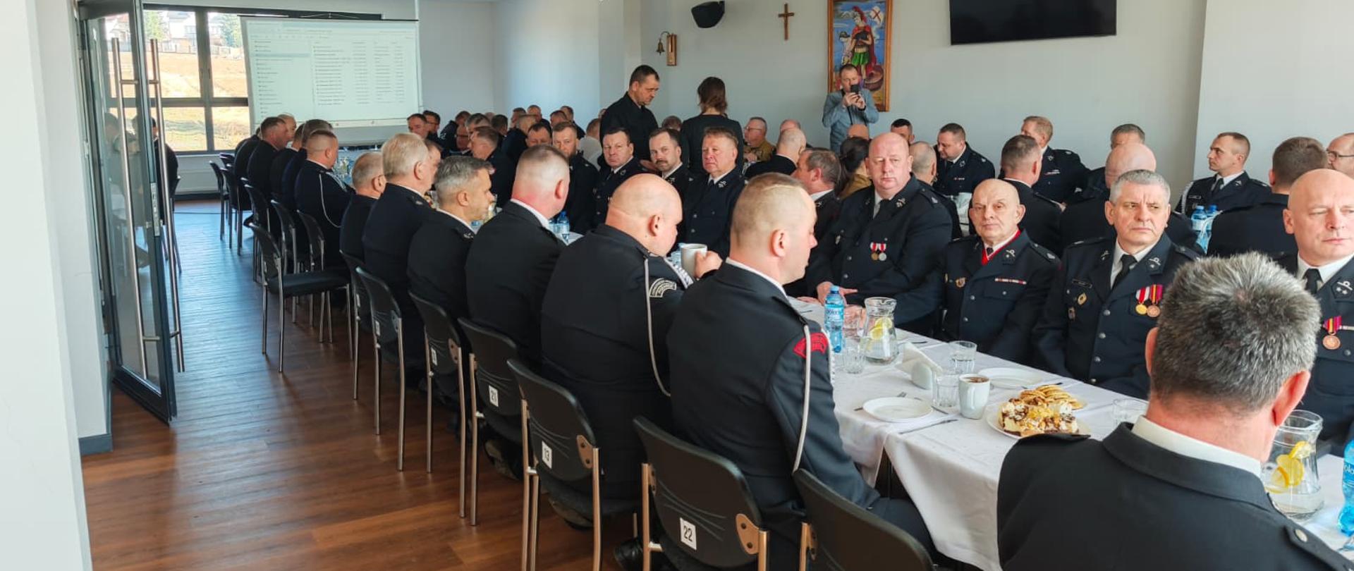 Zdjęcie przedstawia salę wypełnioną uczestnikami narady - prezesami i naczelnikami jednostek OSP powiatu kartuskiego. Strażacy ubrani są w mundury wyjściowe, siedzą przy stole, w tle projektor.