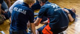 Policjanci podczas nauki praktycznej stabilizacji kończyn dolnych w trakcie części praktycznej kursu kwalifikowanej pierwszej pomocy. Zajęcia odbywały się na sali gimnastycznej KW PSP w Opolu.