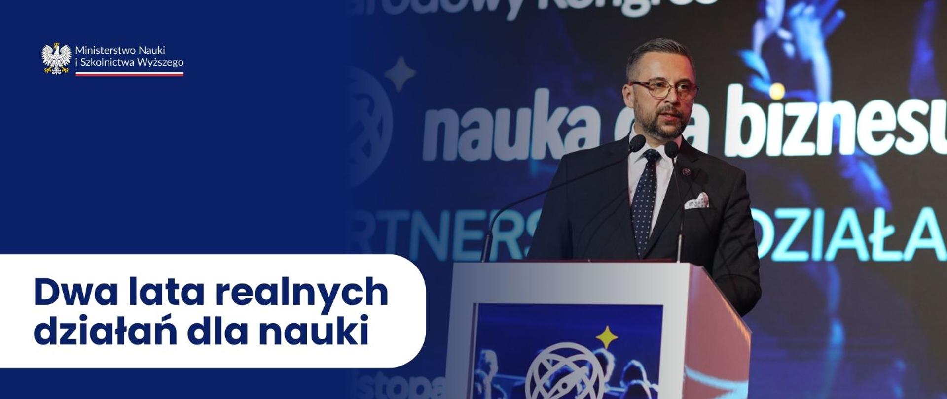Grafika - na niebieskim tle napis Dwa lata realnych działań dla nauki, obok zdjęcie ministra Kulaska stojącego za mównicą.