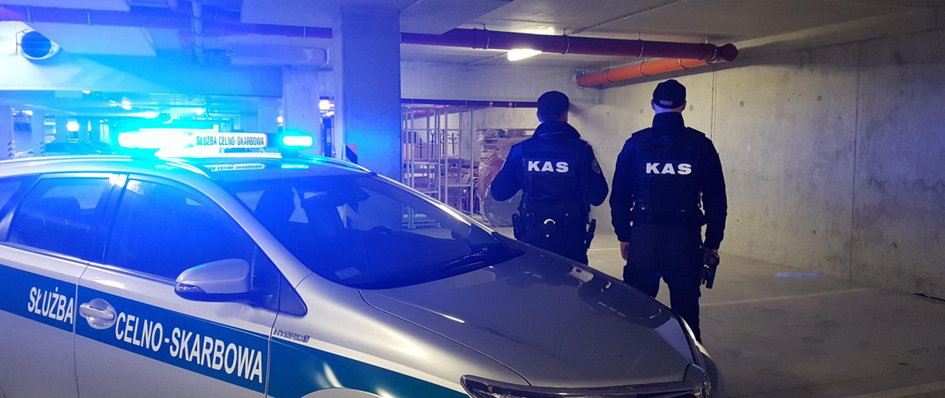 Funkcjonariusze KAS przy radiowozie z załączonym sygnałem świetlnym.