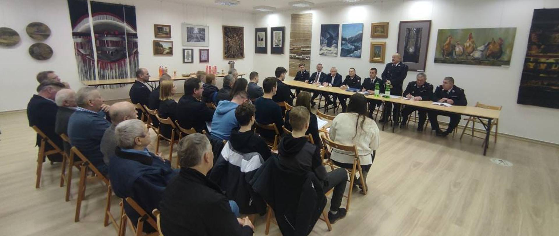 Zdjęcie przedstawia gości, organizatorów i uczestników spotkania sprawozdawczego w jednostce ochotniczej straży pożarnej. 