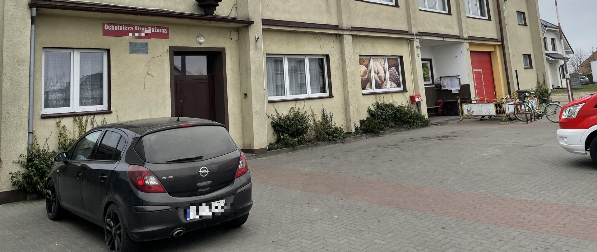 budynek OSP przed którym stoi czarny samochód osobowy widoczny przód czerwonego samochodu