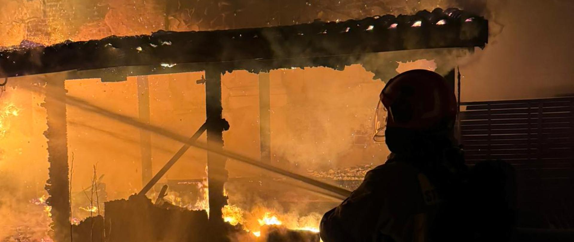 Strażak podający wodę na drewniana zabudowę w ogniu