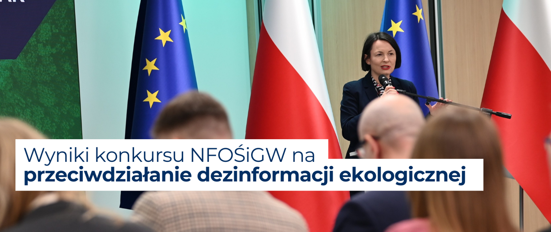 Prezeska Zarządu NFOŚiGW Dorota Zawadzka-Stępniak przemawia do publiczności. W tle flagi Polski i UE. 