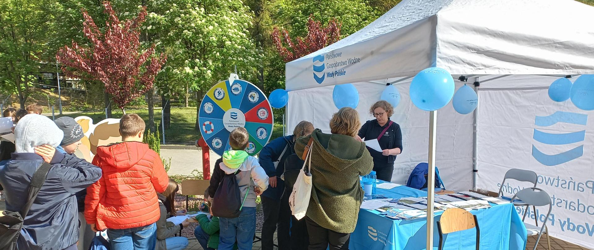 Stoisko firmowe PGW Wody Polskie podczas obchodów Światowego Dnia Ziemi na UMCS w Lublinie. Na pierwszym planie uczniowie- uczestnicy spotkania. 
