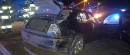 Zdjęcie przedstawia zniszczony samochód osobowy po wypadku, obok stoją strażacy