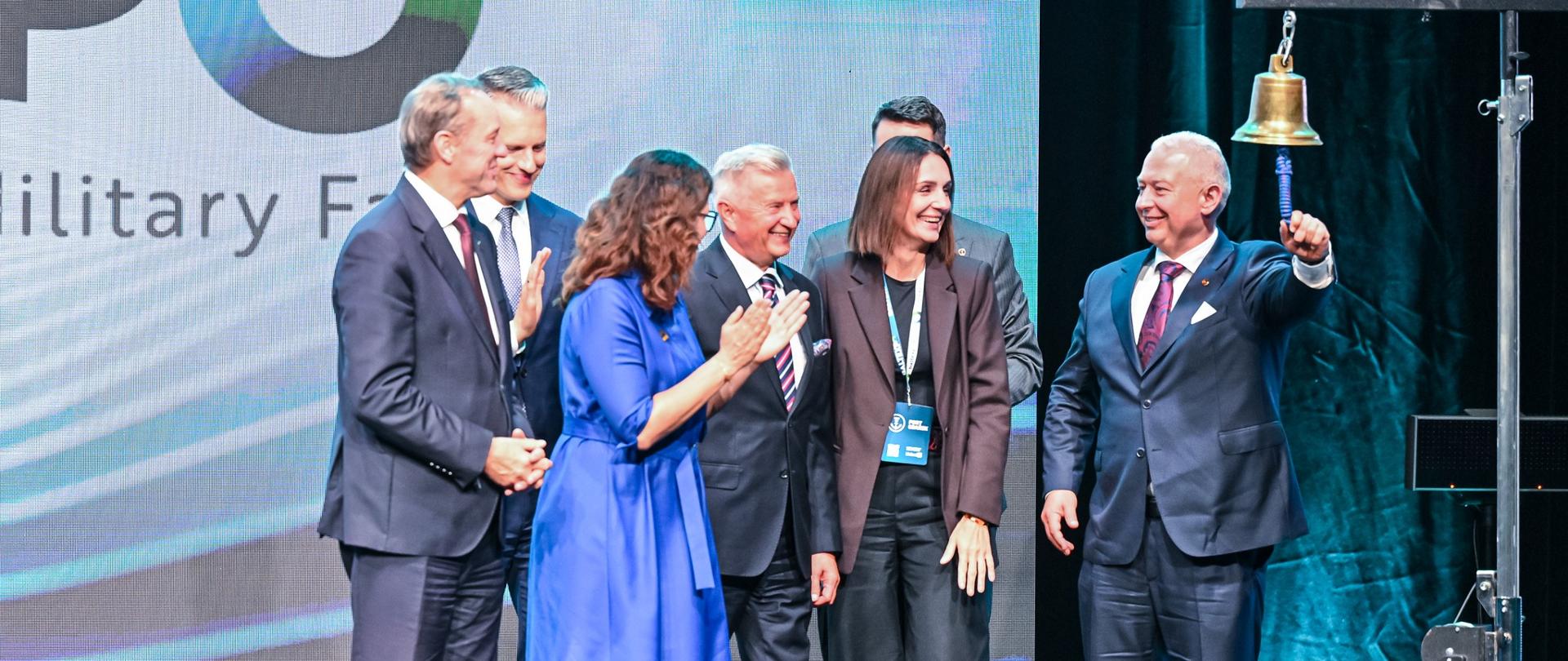 kilka osób stoi na scenie , jedna z nich uderza w dzwon