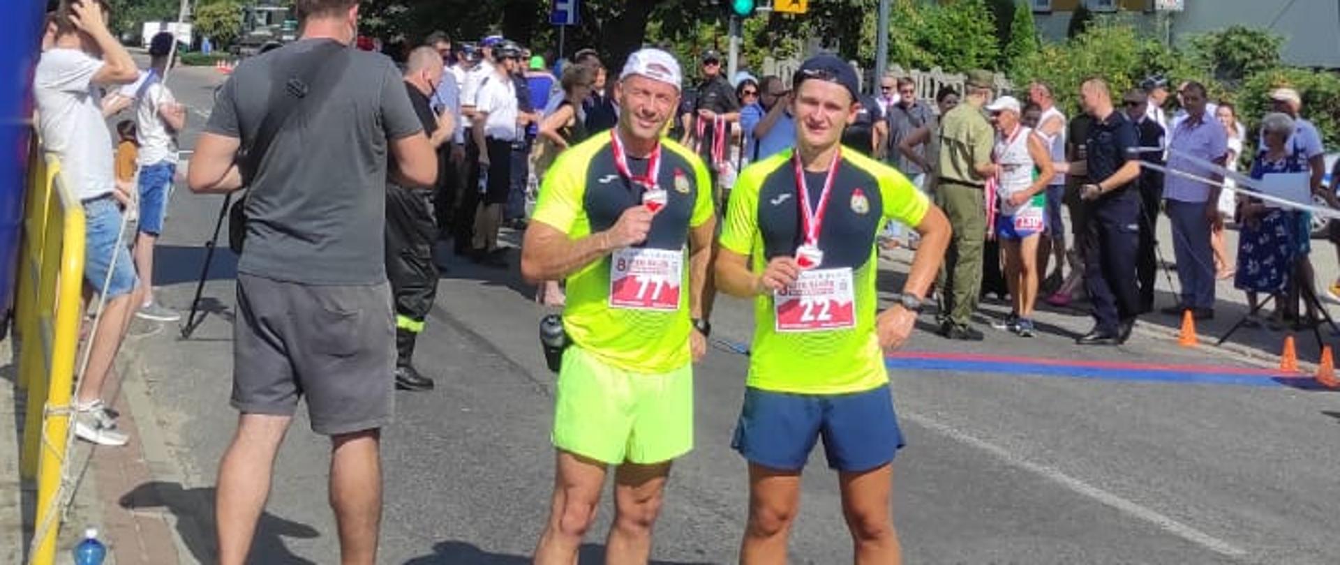 Dwaj funkcjonariusze KP PSP Środa Wielkopolska na mecie biegu. W dłoniach trzymają pamiątkowe medale.