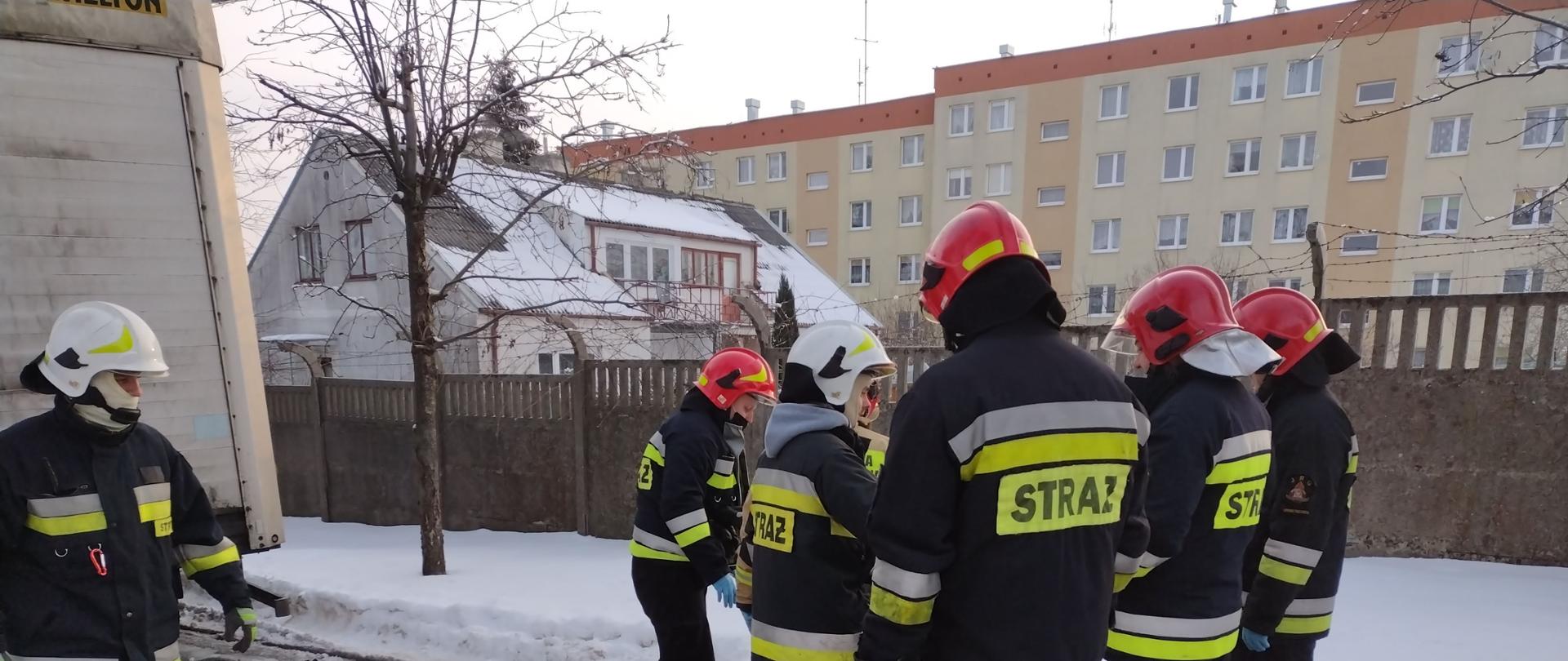 Na zdjęciu strażacy zabezpieczający poszkodowanego mężczyznę. Mężczyzna ocieplony folią życia leży na noszach. W tle przyczepa samochodu ciężarowego