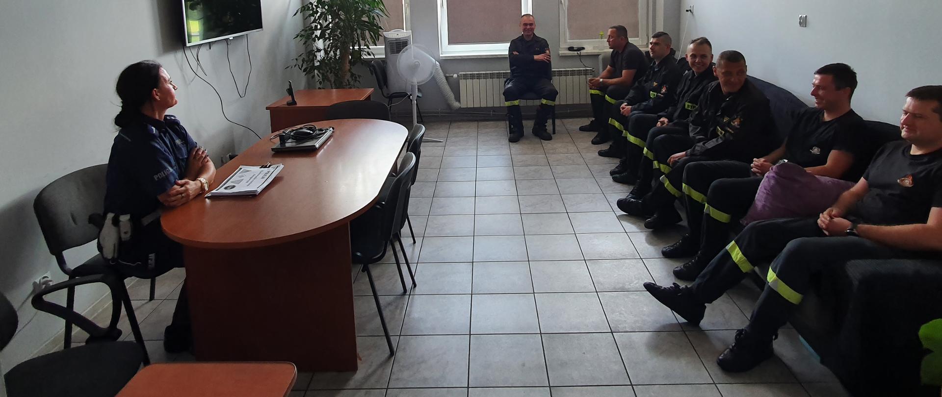 Zdjęcie przedstawia funkcjonariusza Policji i 7 strażaków podczas prelekcji z zakresu bezpieczeństwa w ruchu drogowym