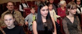 Na widowni w pierwszym rzędzie siedzi dziewczynka i dwie nastolatki, za nimi kilkanaście osób w różnym wieku.