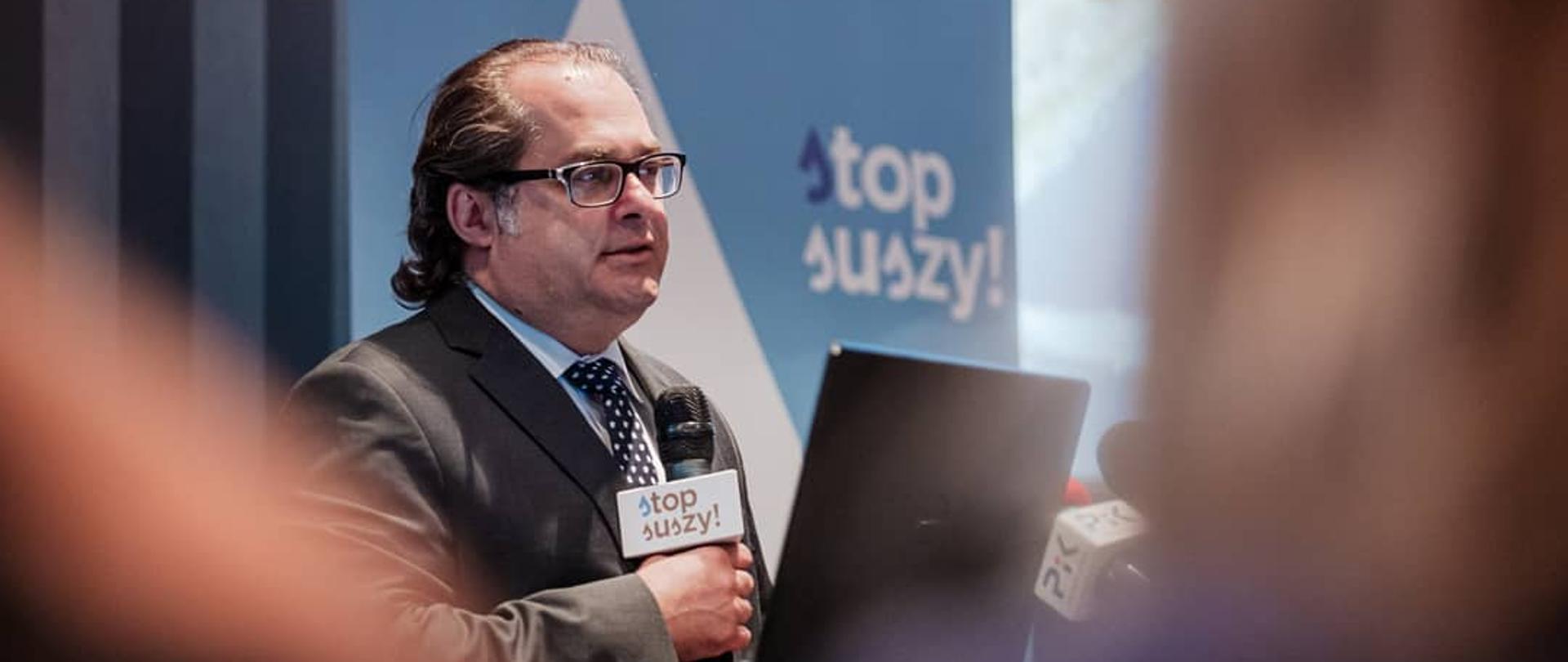 Minister Marek Gróbarczyk przemawia przez mikrofon, w tle baner z hasłem "stop suszy".